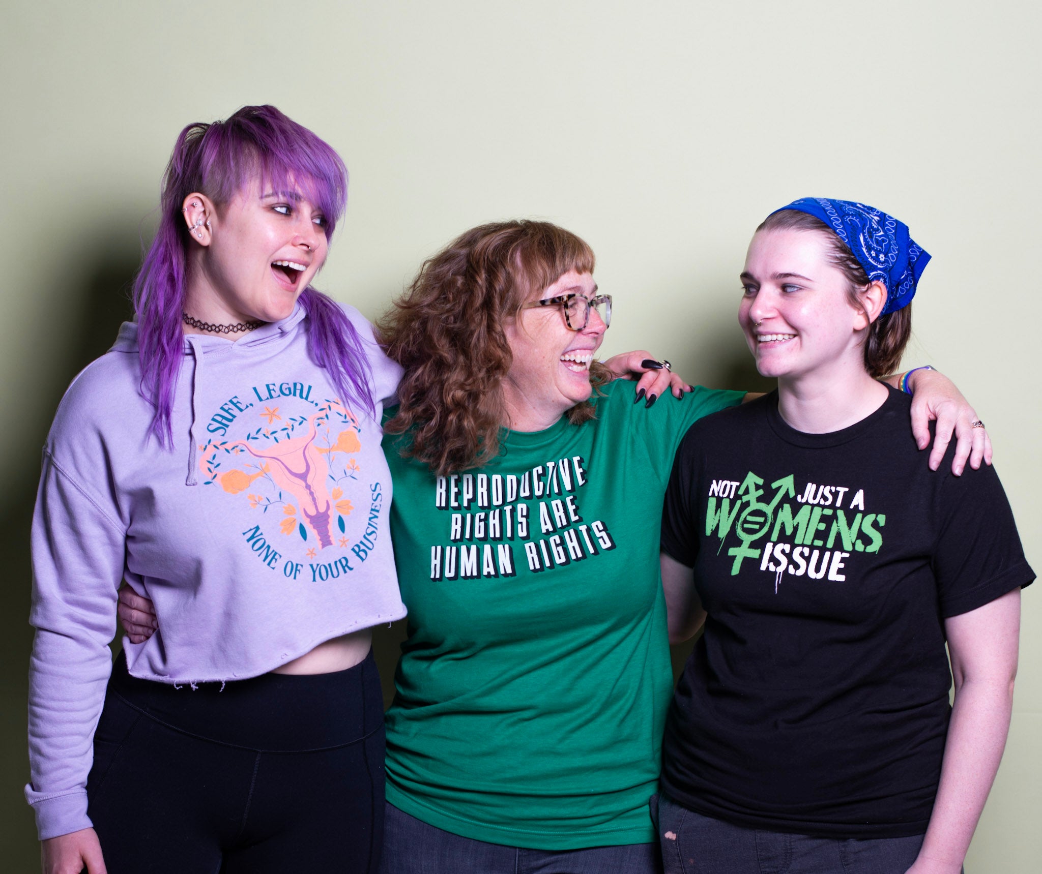 Three women smile at each other while wearing shirts and hoodies from Music City Creative's Reproductive Rights Collection